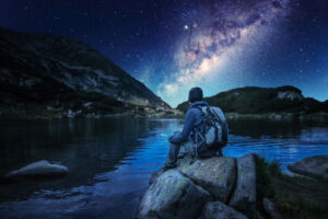 Hiker at mountain lake looking at night sky