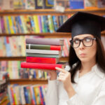 Student with a graduation cap on holding books in one hand and thinking deep